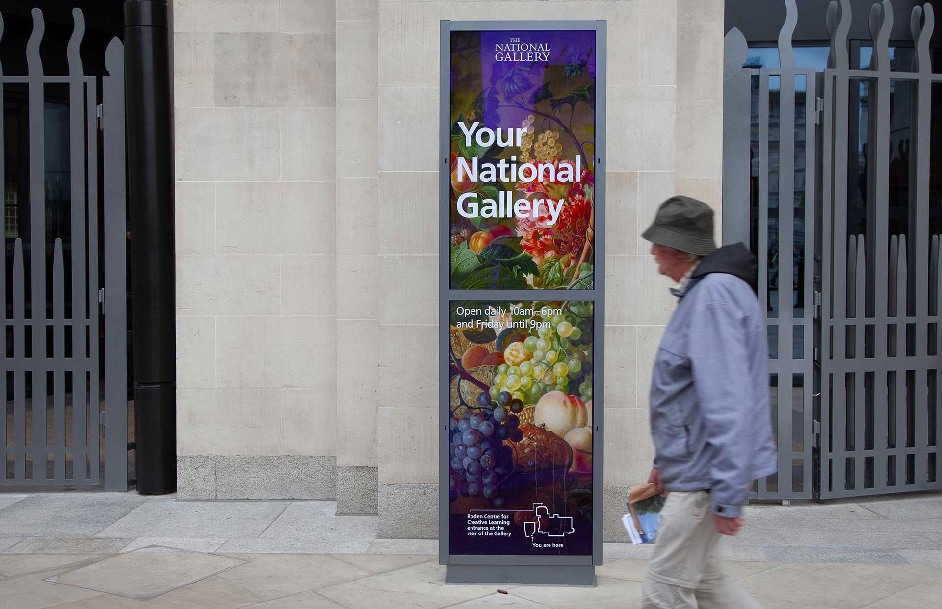 A photograph of a man walking past a digital totem outside the National Gallery in Trafalgar Square