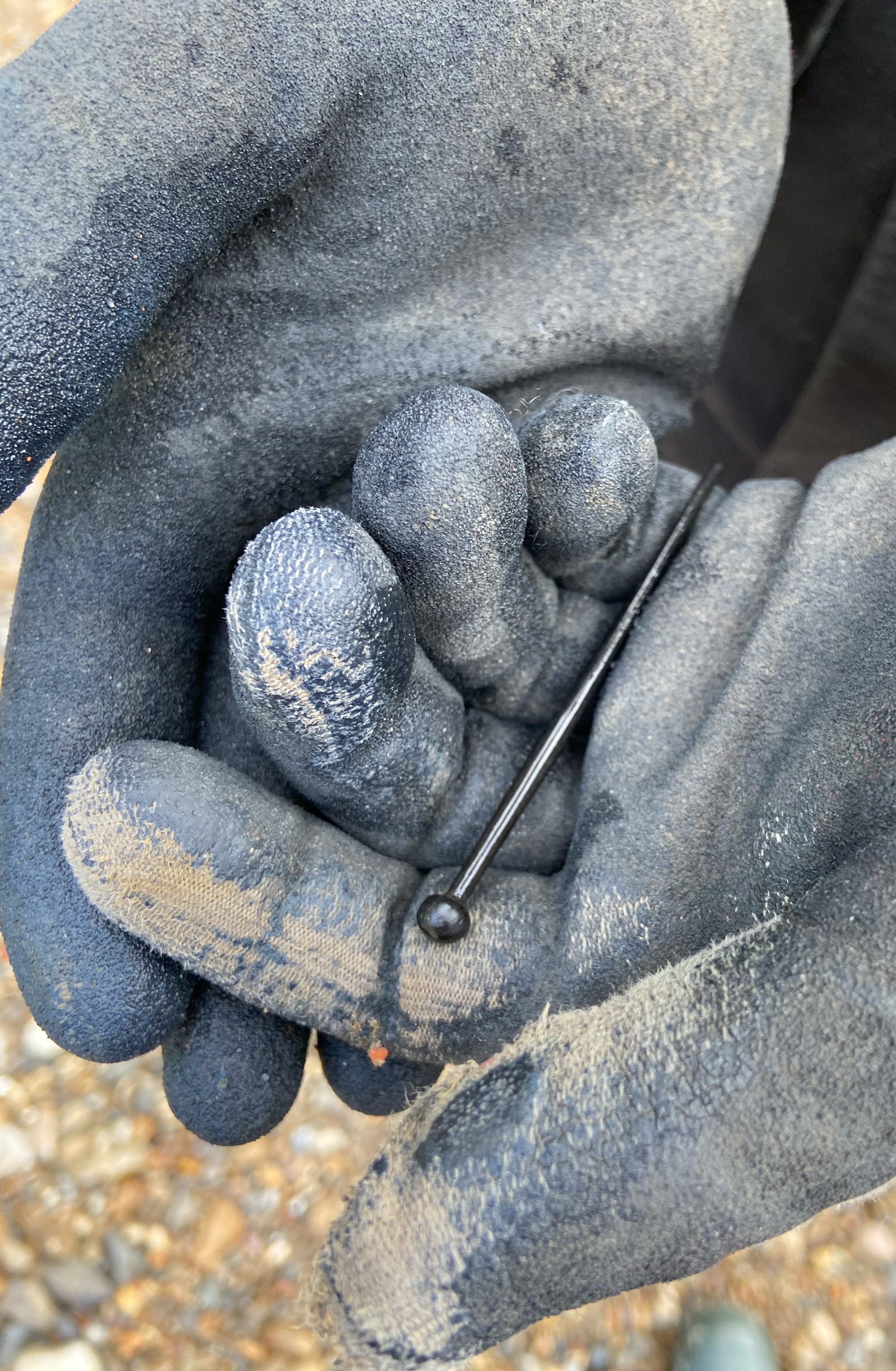 A photo of a gloved hands holding a large black metal pin found on the foreshore of the River Thames