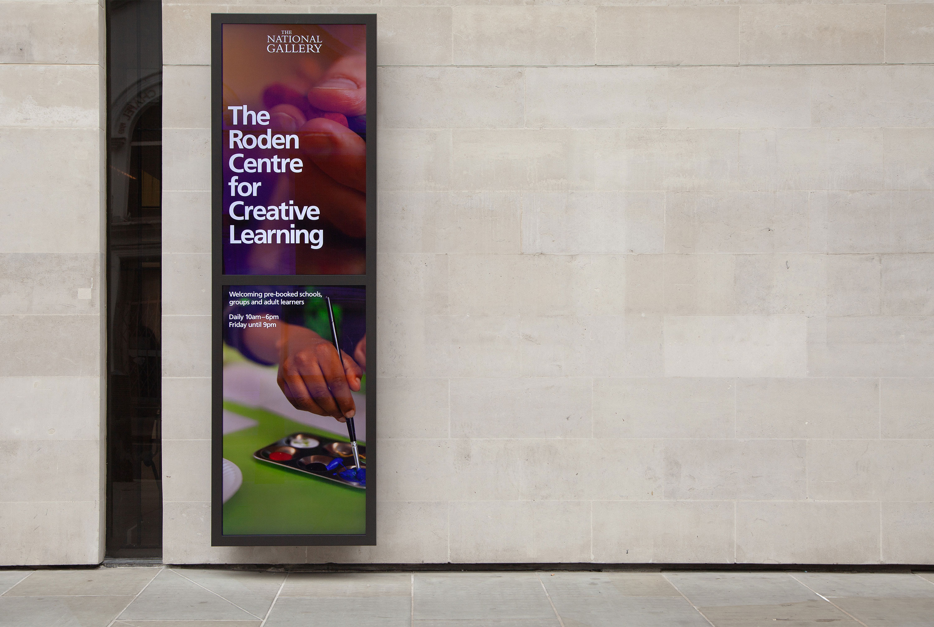 A photo of a tall digital signage totem mounted on the stone wall outside the Roden Centre for Creative Learning at the National Gallery