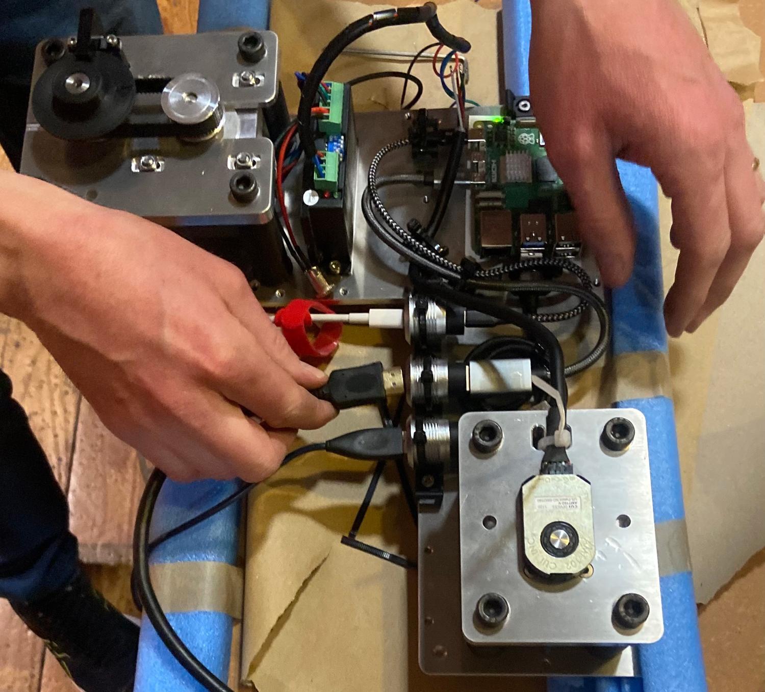 A photo of Tom Cecil assembling the internal workings of the interactive turntable. A close up of two hands plugging cables into electronic and mechanical components.